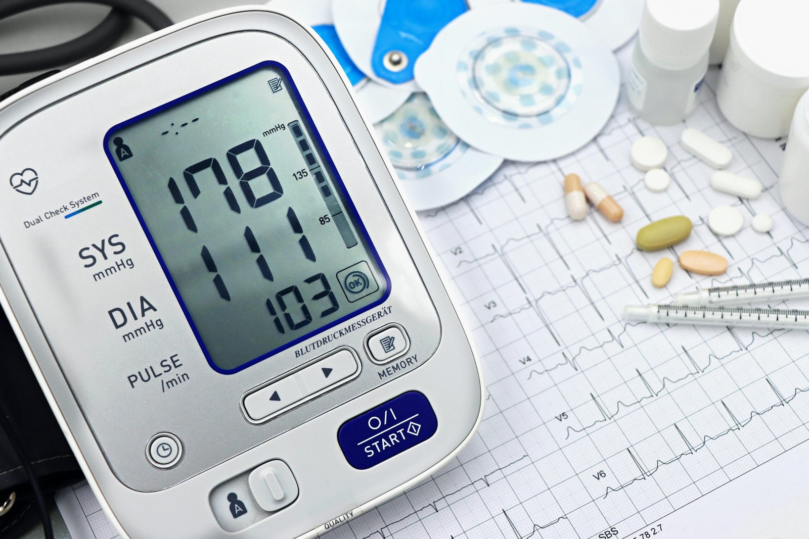 Close-up of a digital blood pressure monitor with ECG printout, pills, and medical tools.
