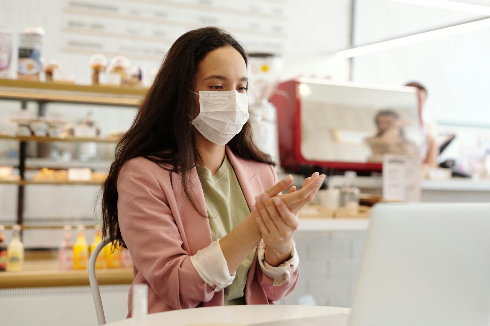 A woman in a mask applies hand sanitizer in a cafe, symbolizing hygiene and safety.