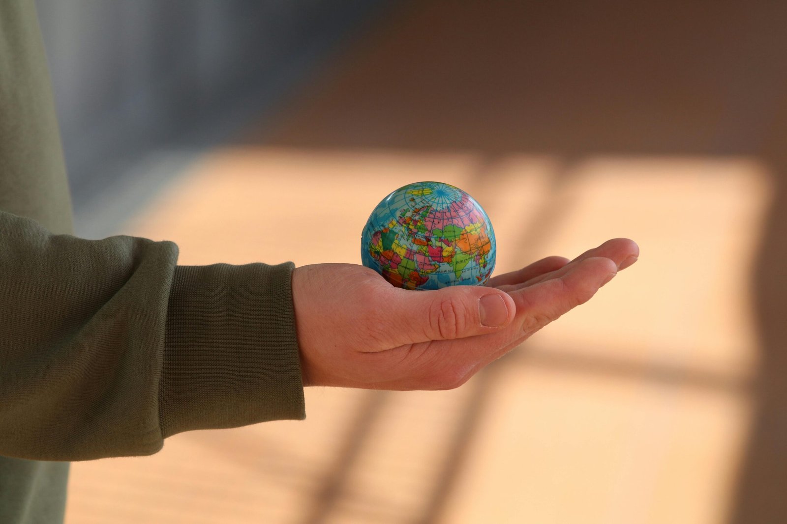 Close-up of a hand holding a small globe with blurred background, emphasizing depth and exploration.
