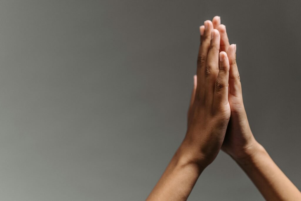Close-up of hands in a prayer gesture against a soft grey background, symbolizing peace and spirituality.