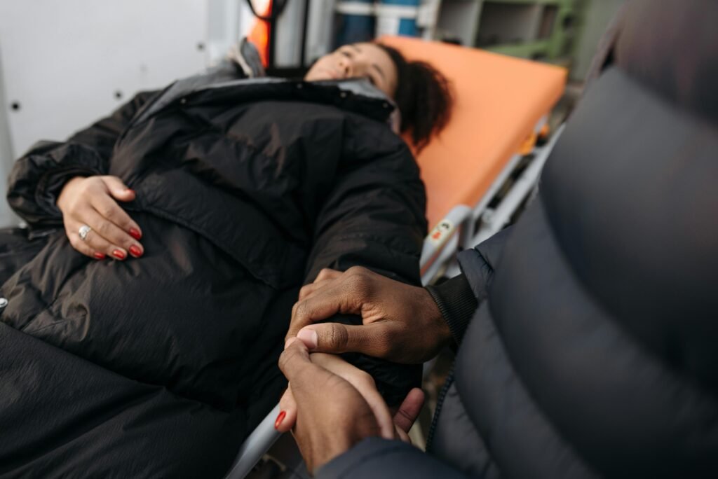 A woman lying on a stretcher as a comforting hand holds hers. Indoor medical care scene.